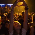 woman at crowd raising her hand while making heart sign