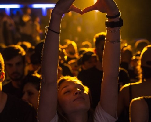 woman at crowd raising her hand while making heart sign